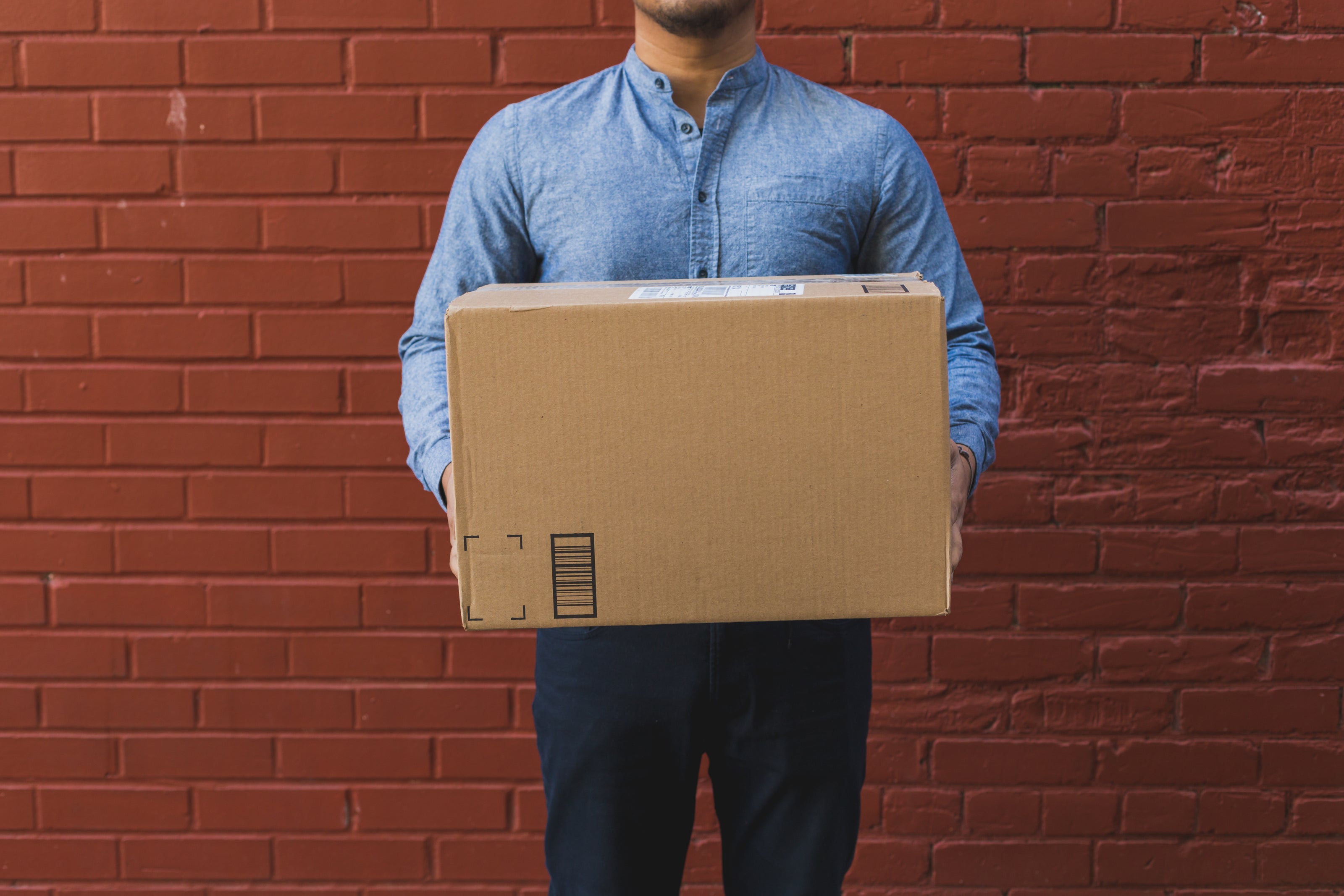 man-holding-shipping-box-on-red-brick - Cottage Toys